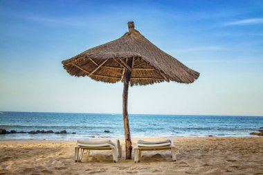 Güneşli bir çift güneş yatağı ve temiz denizin yakınındaki boş kumsalda şemsiye. Senegal, Afrika 'da tropik bir cennettir. Mavi gökyüzü var. Rahatlamak ve dinlenmek için doğru yer..