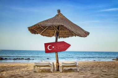 Ahşap ok tabelası üzerinde Türk bayrağı. Plajda iki şezlong ve bir güneş şemsiyesi vardır. Bu açık bir deniz ile tropikal bir cennet.
