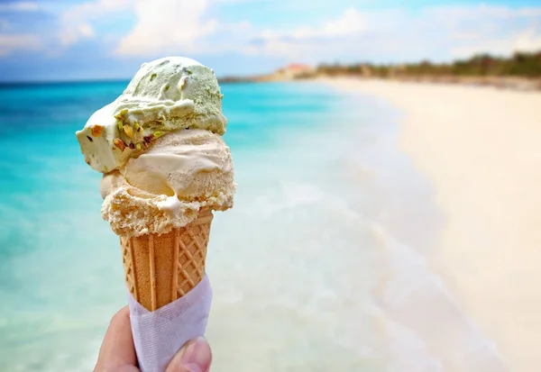 A mão está a segurar o gelado de baunilha. No fundo é o céu azul, mar nd praia de areia. Este está situado em resort tropical . — Fotografia de Stock