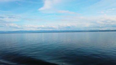 Constance Gölü, Bodensee 4k video. Yatlar gölde yelken açar. Su kristal mavisi ve arkasında yüksek karlı Alpler duruyor. Mavi gökyüzünde bulutlar var..