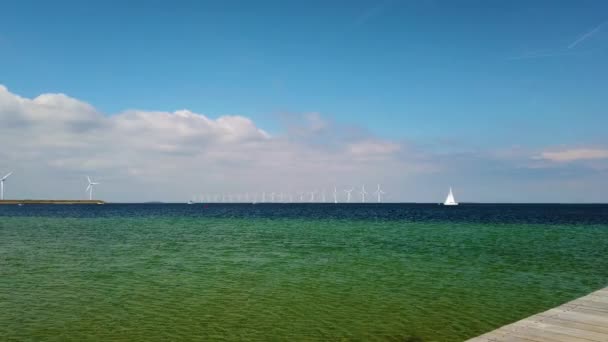 4K video of White windmills stand on the clear turquoise North Sea. A luxury yacht is slowly passing by them. It is in Copenhagen. — Stock Video