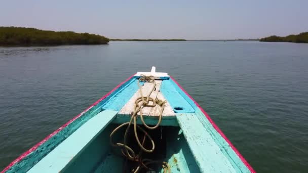 4K video of Wooden blue and white canoe floats on water surface. It is a sea lagoon in Africa, Senegal. It is birds national park. The background is clear water and blue sky. — Stock Video