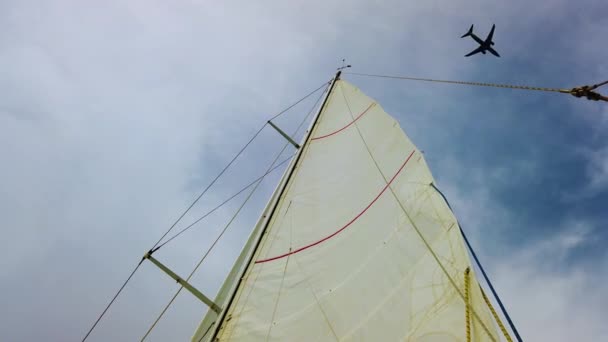 4k Video Ansicht von Segel auf Jacht in Italien. über dem Schiff fliegt das Flugzeug. Das Segel ist groß und weiß. Der Wind bläst und die Jacht schwimmt in den Wellen. es ist auf See vor der Insel Sardinen. — Stockvideo