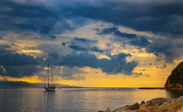 Kapal pesiar di laut Mediterania saat matahari terbit, Cagliari, Italia. Orang-orang berlayar di kayak di laut terbuka di bawah matahari. Matahari menerangi pulau dengan warna emas yang indah . — Stok Foto