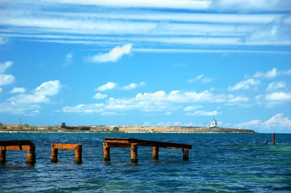 Jembatan logam yang rusak di laut terbuka dengan langit biru — Stok Foto
