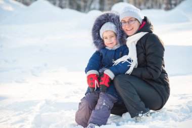 Çekici küçük kız, yürüyüş sırasında kırsal kesimde kışlık giysiler içinde pozitif annesiyle poz veriyor. Kırsalda kış tatili kavramı