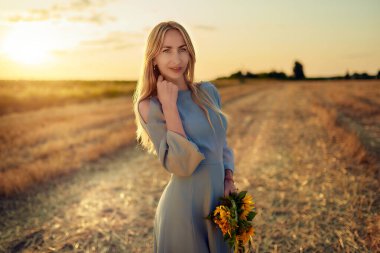 Mutlu, genç, güzel, sıska bir kadın, güneşli bir yaz akşamında gururlanmak için elinde bir buket ayçiçeği ve sepetle tarlada yürür. Doğadan zevk alma kavramı