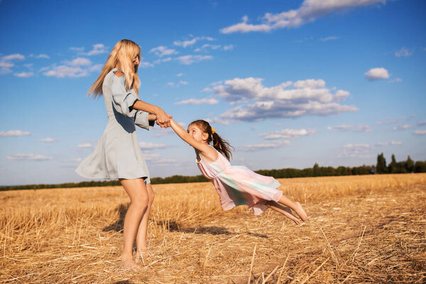 Cheerful young mother is spinning her cute little daughter while walking on a field with mowed wheat on a sunny warm summer day. The concept of unity with nature