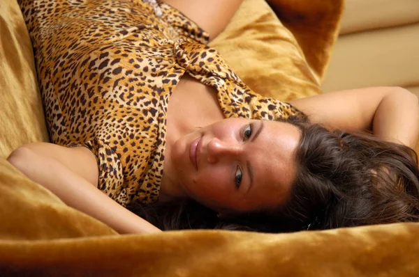 Gyönyörű nő pózol egy bőr kanapén egy elbűvölő tigris ruhában. — Stock Fotó