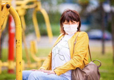 Kimliği belirsiz orta yaşlı kadın koruyucu beyaz bir tıbbi maskeyle bahar parkında yürüyor. Coronovirus koruma kavramı