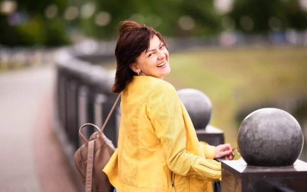 Beautiful well-groomed energetic middle-aged woman posing coquettishly while the sun while walking around the city in summer. Concept of middle-aged women their concerns and health.