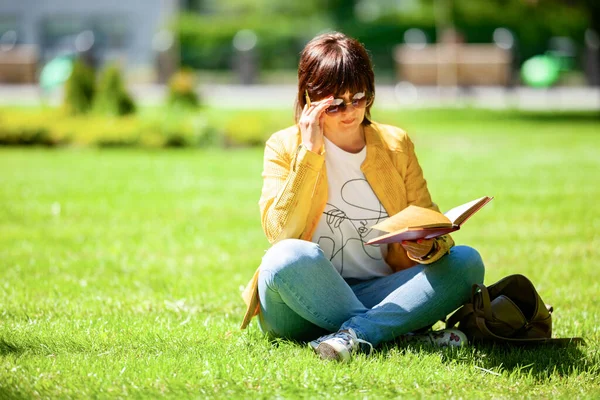 Pozytywna Kobieta Średnim Wieku Okularach Przeciwsłonecznych Siedzi Polu Parku Czyta — Zdjęcie stockowe