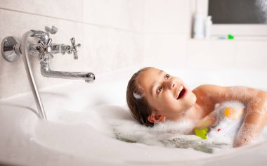 Komik küçük kız küvette şişme bir can simidiyle ve suda köpükle banyo yapıyor. Çocuklar için hijyen ve eğlence kavramı. Reklam alanı