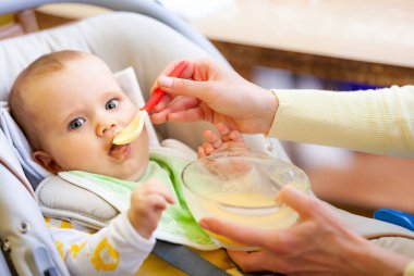 Tanımlanamayan annelerin eli, yeni doğmuş şirin bir kızı bebek mamasıyla dikkatlice besler. Çocuklar için çocuk bakımı ve kaliteli ürünler kavramı