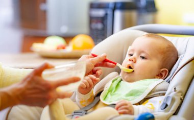 Küçük, akıllı bir kızın bebek koltuğunda oturup, anneye bakarken bir oyuncağı kemirmesinin yan görüntüsü. Uygun duygusal gelişim ve çocuk sağlığı kavramı