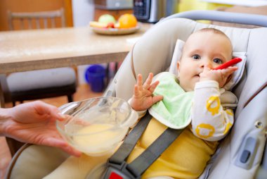 Küçük, akıllı bir kızın bebek koltuğunda oturup, anneye bakarken bir oyuncağı kemirmesinin yan görüntüsü. Uygun duygusal gelişim ve çocuk sağlığı kavramı