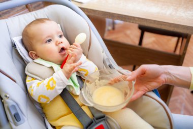 Sevimli, memnun, beyaz, altı aylık bir kız çocuk koltuğunda oturup sevgili çıngıraklı çıngırağıyla oynuyor. Sağlık ve kaliteli bebek ürünleri kavramı