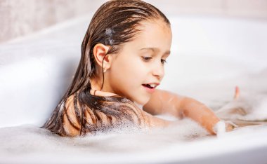 Küçük beyaz kız köpükle küvette banyo yapıyor ve evde karantina sırasında eğleniyor. Hijyen ve çocuk sağlığı konsepti. Kopyalama alanı