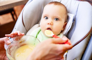 Tanımlanamayan annelerin eli, yeni doğmuş şirin bir kızı bebek mamasıyla dikkatlice besler. Çocuklar için çocuk bakımı ve kaliteli ürünler kavramı