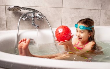 Mayo giymiş gülümseyen küçük kız banyoda banyo yaparken top oynamaktan hoşlanıyor. Aile kavramı, koronovirüs çağında dinleniyor. Kopyalama alanı
