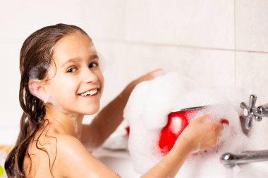 Neşeli küçük beyaz kız karantina sırasında küvette banyo yaparken köpükle oynuyor. Komik çocuklar Coronavirus sırasında evde eğlenirler. Kopyalama alanı