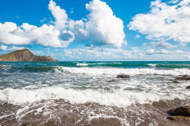 Arkasında dağlar olan kumsal. Dağlar çimlerle kaplıdır ve denizden dik kayalıklara sahiptir. Gökyüzü bulutlu