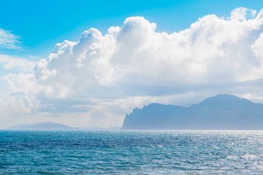 Arkasında dağlar olan kumsal. Dağlar çimlerle kaplıdır ve denizden dik kayalıklara sahiptir. Gökyüzü bulutlu