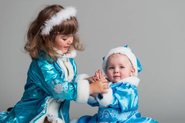 Snow Maiden kostümlü sevimli küçük kızların ön görüntüsü. Elinde portakal ve şeker tutan gülümseyen çocuklar. Mavi stüdyo arka planında izole edilmiş. Yeni yıl tatili kavramı.