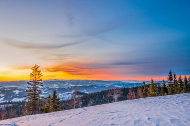 Dağ vadisinde gün batımının ve bulutlu mavi gökyüzünün arkaplanına karşı ladin ormanları ve kar yığınlarıyla huzur verici bir manzara. Açık hava eğlencesi kavramı. Reklam alanı