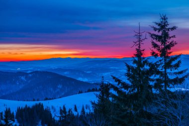 Dağ vadisinde gün batımının ve bulutlu mavi gökyüzünün arkaplanına karşı ladin ormanları ve kar yığınlarıyla huzur verici bir manzara. Açık hava eğlencesi kavramı. Reklam alanı