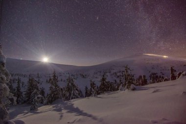 Kış mevsiminde bir dağ vadisinde karlı tepelerin mistik manzarası sisli bir gökyüzü ile batan altın güneşe karşı. Kırsal kesimde yürüyüş ve kayak merkezi kavramı