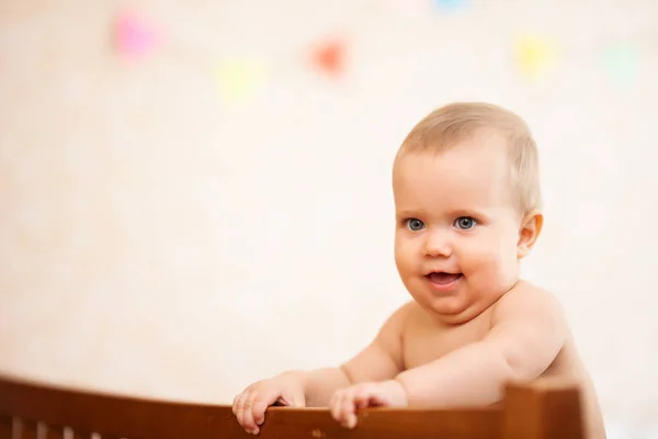 快乐的小宝宝站在室内的木制婴儿床上 装饰着婴儿房 从侧面看可爱的赤裸裸的高加索小孩张着嘴笑 幸福童年的概念 — 图库照片