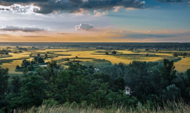 Etkileyici yaz günbatımı gökyüzü, boş tarım arazileri, yeşil çayırlar, ağaçlar ve küçük göller. Muhteşem doğa manzarası, uçsuz bucaksız tarlalar taze çimenler ve ormanlar..