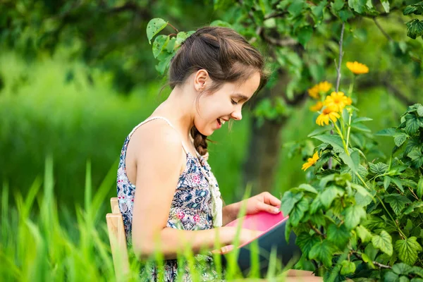 Kahverengi örgülü beyaz kadın gencin seçici odağı çalılık ve çiçeklerin yanındaki ahşap sandalyede oturuyor. Kırsal kesimde hasat toplayan çiftçi kız manzarası.