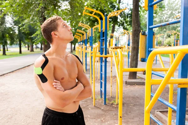 Spor sahasında poz veren siyah ve yeşil bantlı yakışıklı, beyaz, profesyonel vücut geliştirici portresi. Çıplak kaslı bir adam yan bakıyor, kollarını kavuşturmuş..