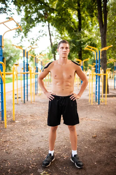 Spor sahasında poz veren siyah ve yeşil bantlı yakışıklı, beyaz, profesyonel vücut geliştirici portresi. Çıplak kaslı bir adam yan bakıyor, kollarını kavuşturmuş..