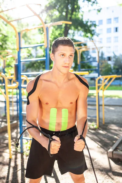 Spor sahasında kaslı adam eğitimi. Vücut eğitiminde elastik kineziyolojisi olan genç yakışıklı vücut geliştiricinin portresi, kameraya bakıyor. Rehabilitasyon kavramı.