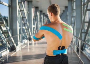 Sırtında Kinezyoloji bandı olan bir adam içeride poz veriyor..