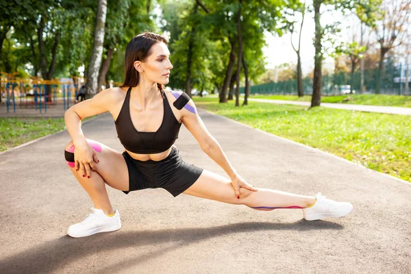 Femeie flexibilă cu bandă kinesiologică care practică plămânii în aer liber . — Fotografie, imagine de stoc
