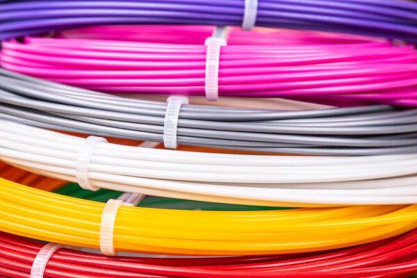 Bunch of colorful rolled cables. Closeup of plastic bright wires for 3D printer lying indoors, white studio background. Concept of children's entertainment and creativity.