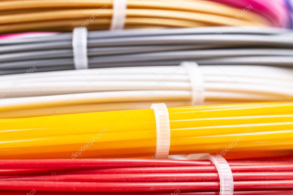 Bunch of colorful rolled cables. Closeup of plastic bright wires for 3D printer lying indoors, white studio background. Concept of children's entertainment and creativity.