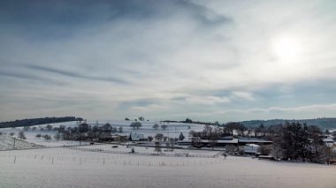 Kar, eski küçük bir köyü ahşap evler ve tarım çiftlikleri ile kapladı. Kel ağaçlarla kaplı tepelik bir bölgede kış bulutlu havalarda. Video 4K UHD zaman ayarlı