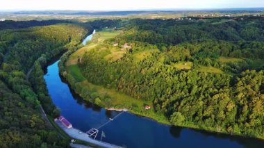 Kupa nehri, Hırvatistan ve Slovenya 'nın yeşil yaprak döken ormanları arasında güneşli bir gökyüzü ve dağların arka planına karşı otoyolun yanında akar. 4K UHD video gerçek zamanlı