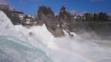 Hızlı fırtınalı soğuk su damlaları düşer ve küçük damlalar Rhine Şelaleleri 'ne İsviçre' deki eski kasabanın arka planına doğru farklı yönlere dağılır. 4k video yavaş çekim UHD