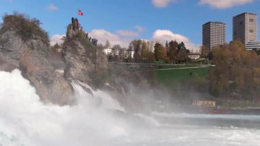 Hızlı fırtınalı soğuk su damlaları düşer ve küçük damlalar Rhine Şelaleleri 'ne İsviçre' deki eski kasabanın arka planına doğru farklı yönlere dağılır. 4k video yavaş çekim UHD