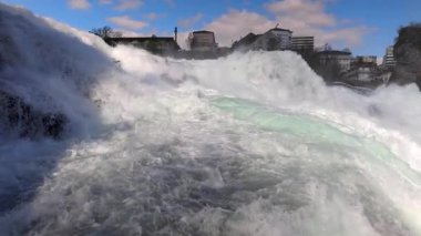 Hızlı fırtınalı soğuk su damlaları düşer ve küçük damlalar Rhine Şelaleleri 'ne İsviçre' deki eski kasabanın arka planına doğru farklı yönlere dağılır. 4k video yavaş çekim UHD