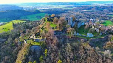 Üzerinde tarihi Hohentwil kalesinin kalıntıları olan yüksek yeşil ağaçlık bir tepenin havadan görünüşü güneş ışığında mavi bir gökyüzüne karşı Singen şehriyle çevrilidir. Video 4k UHD eş zamanlı