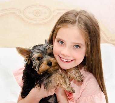Holding ve köpek yavrusu yorkshire terrier ile oynayan sevimli gülümseyen küçük kız çocuğu 