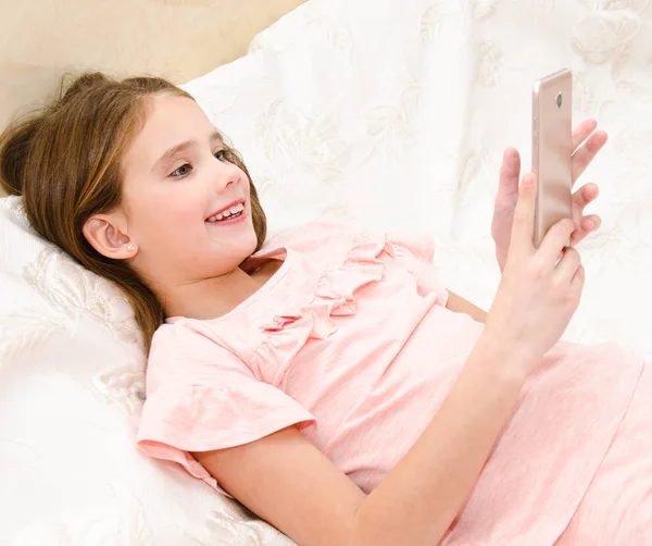 Симпатичная Улыбающаяся Маленькая Девочка Смартфоном Мобильного Телефона Лежащим Кровати — стоковое фото