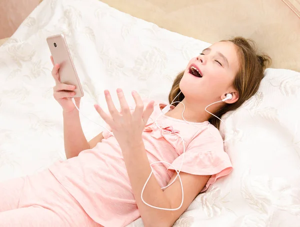 Ładna Dziewczynka Leżąc Łóżku Słuchając Muzyki Śpiewu Pomocą Smartfona Słuchanie — Zdjęcie stockowe